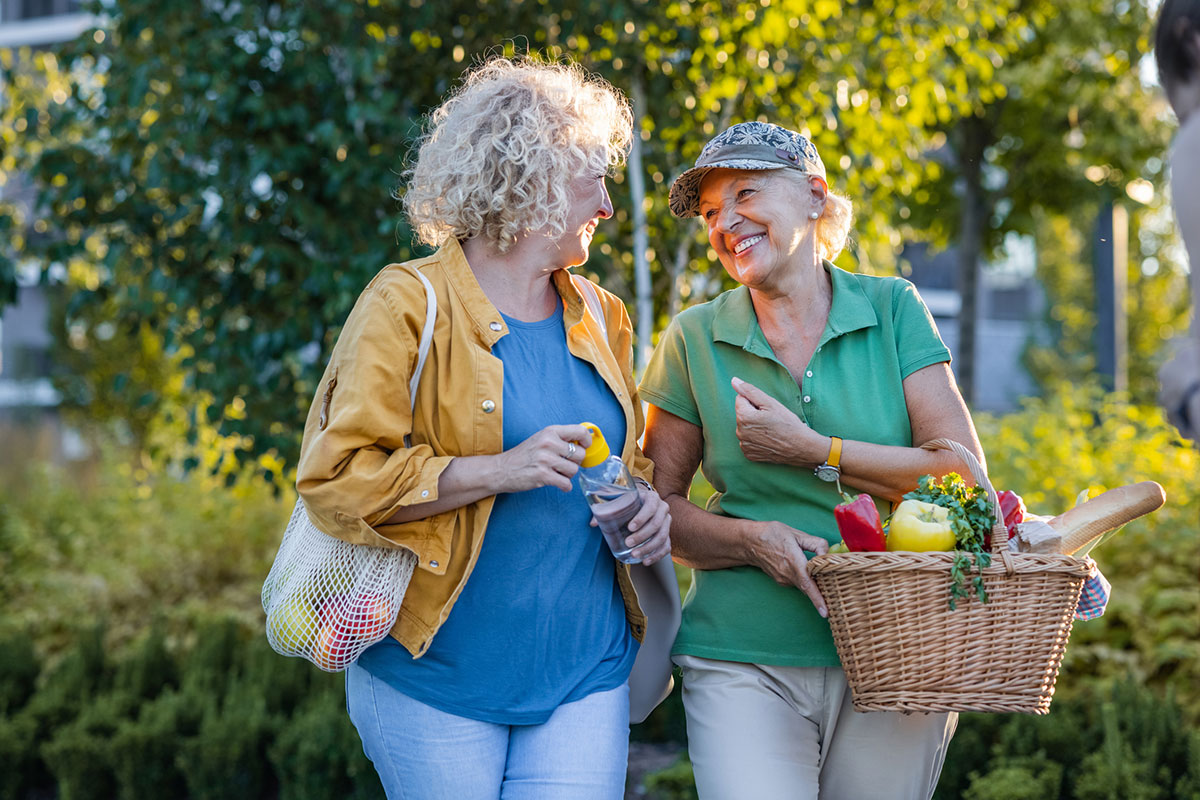 two senior women walking on a sunny day carrying a basket of vegetables
