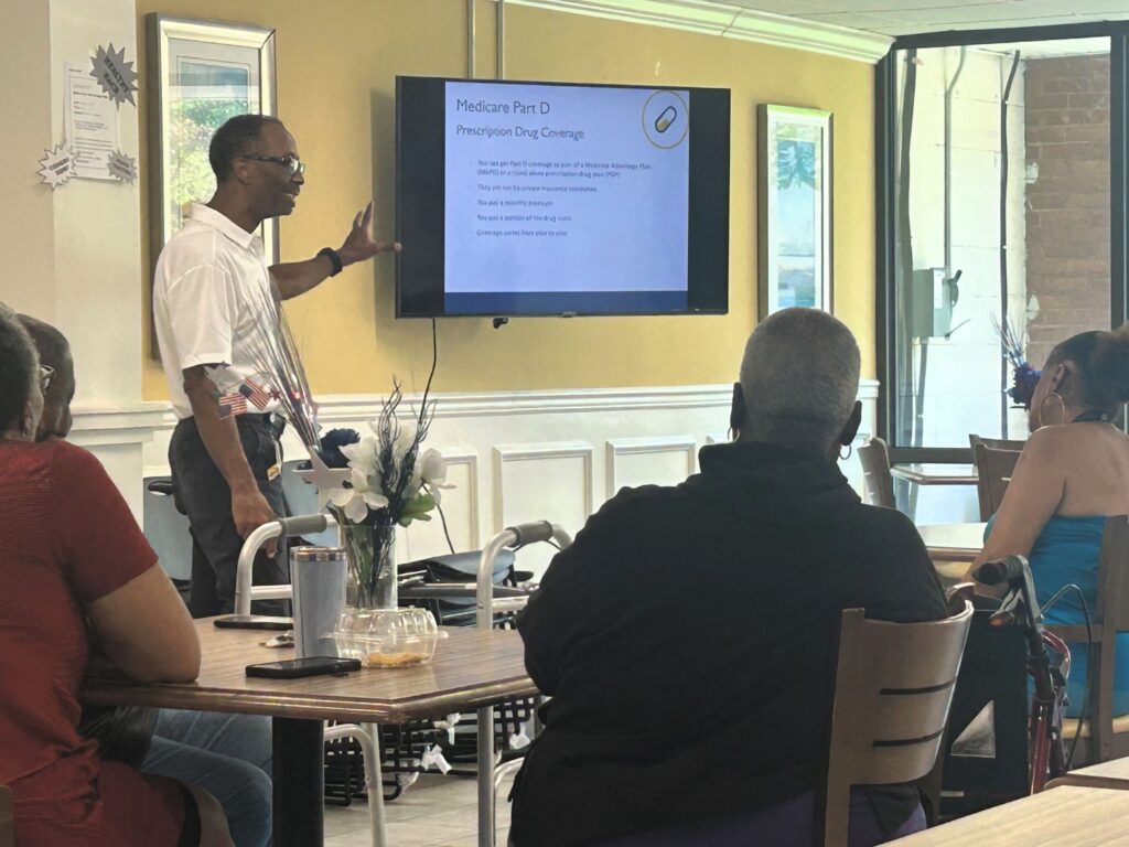 A Johns Hopkins Advantage MD representative presents a Medicare 101 seminar to Bowman Place residents, with a slide on prescription drug coverage displayed.