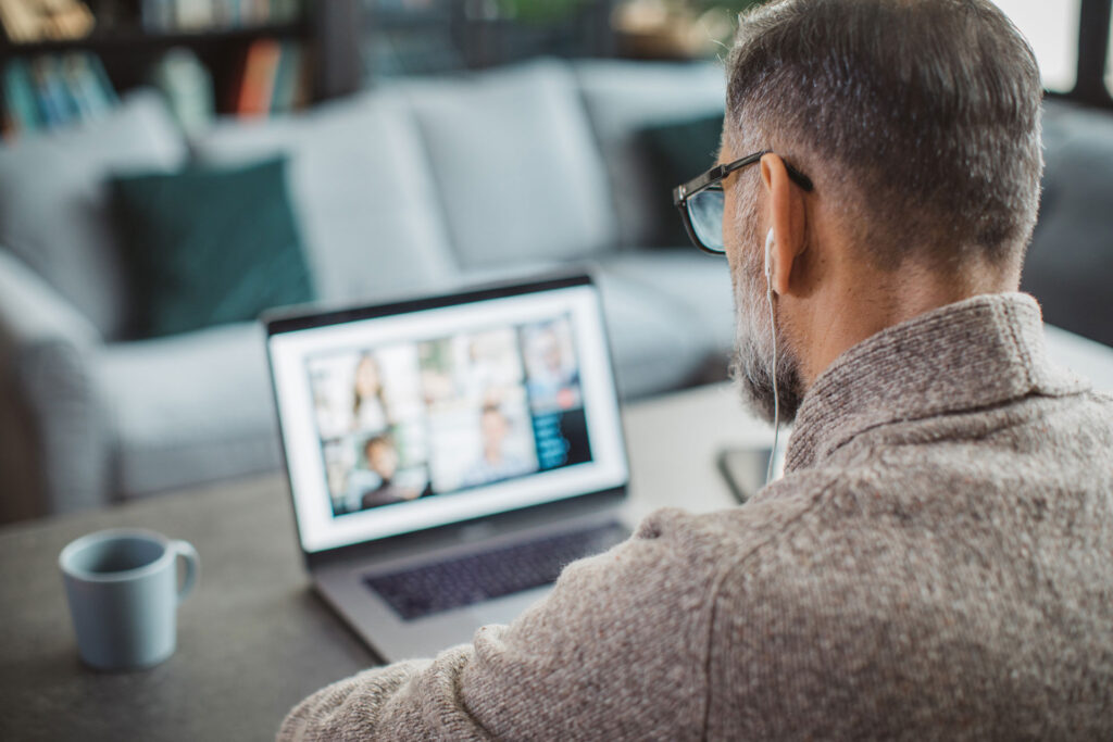 Mature male sitting at a desk with head phones watching a video on laptop